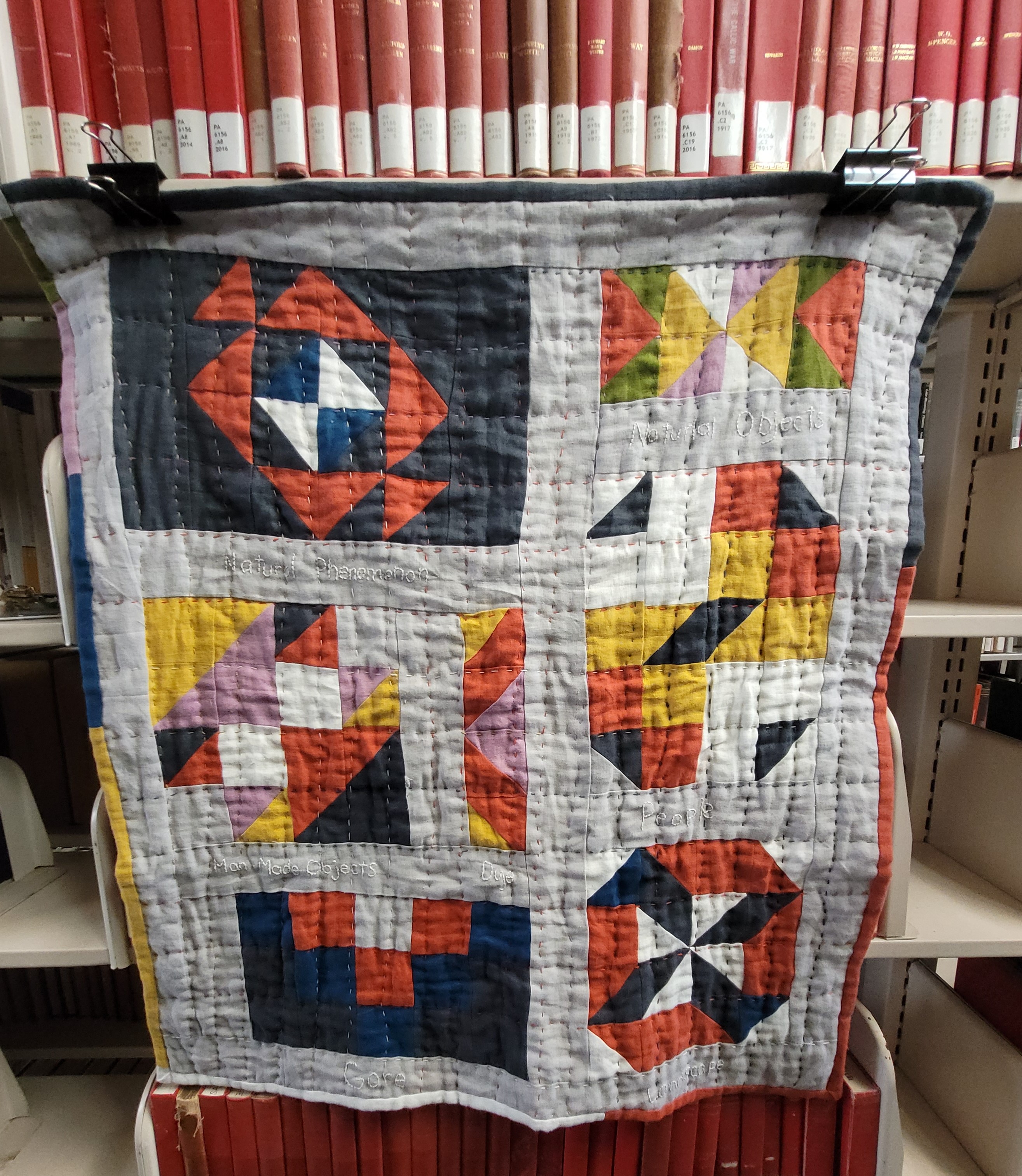 a modern patchwork quilt hanging from a library shelf